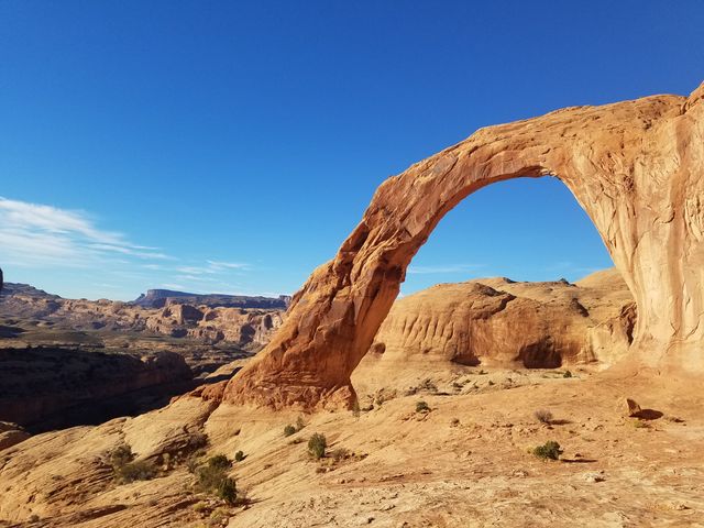 A natural arch in Moab, Utah next to mountains. 