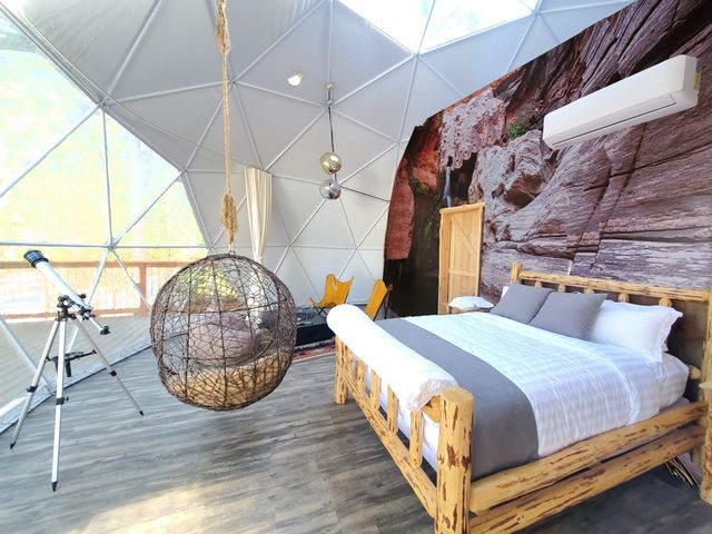 A geodesic dome with a bed, a hanging chair, rock-themed wallpaper, and a telescope