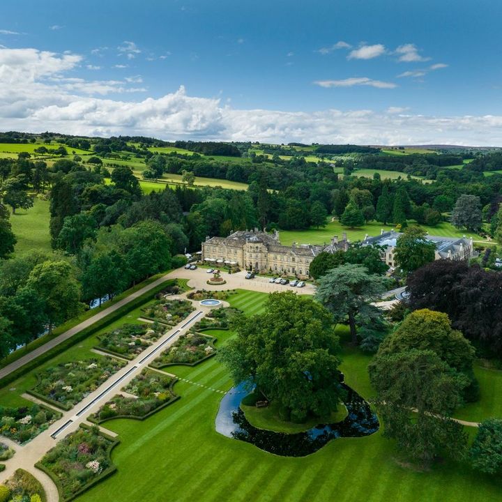 An English countryside estate-turned-hotel as seen from above surrounded by green lawns, bushes, and lush landscaping.