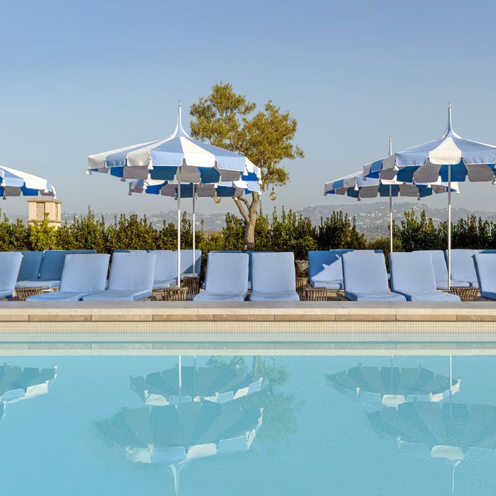 The rooftop pool at the Maybourne Beverly Hills with rows of white chairs, blue and white striped umbrellas, and LA views.