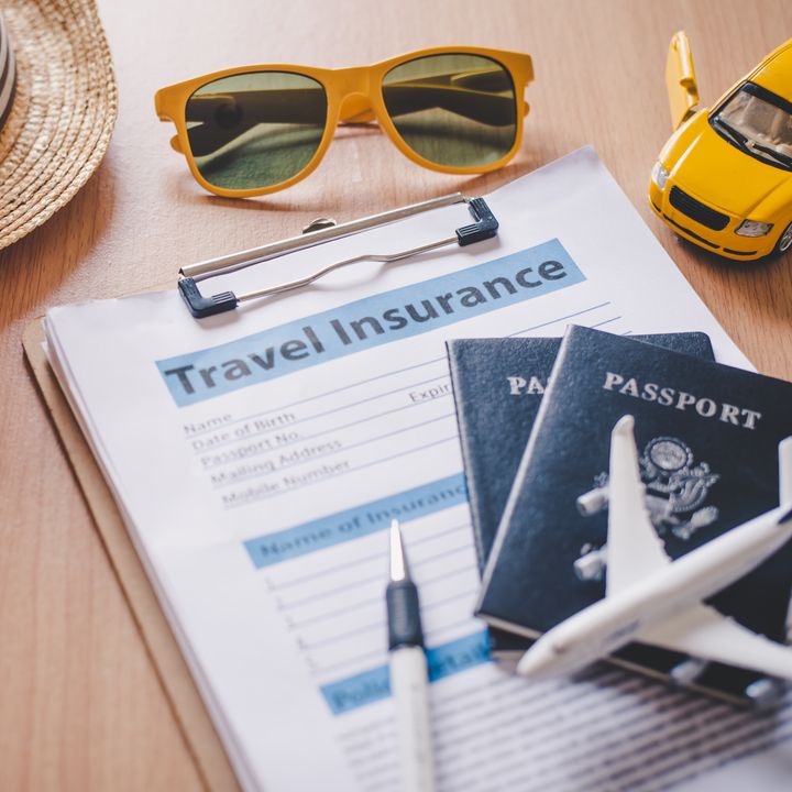 A clipboard with travel insurance paperwork plus passports, a pen, sunglasses, a hat, starfish, and toy plane and car.