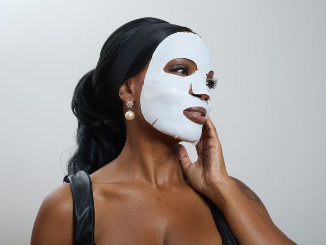 A woman poses with a sheet face mask covering her face.