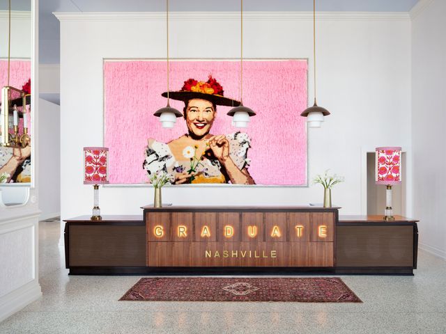 A hotel check-in desk that says Graduate Nashville with a painting behind it of a cheerful person.