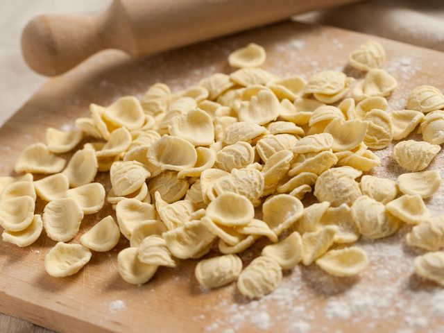 A wooden board covered with oriechette pasta dusted with flower.
