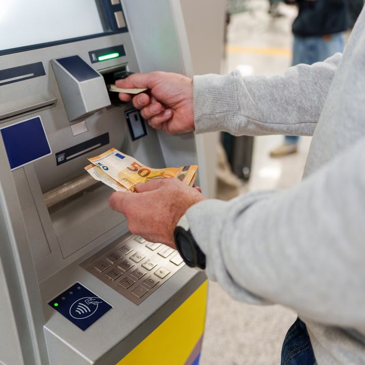 A person at an ATM with only arms visible taking out Euros.