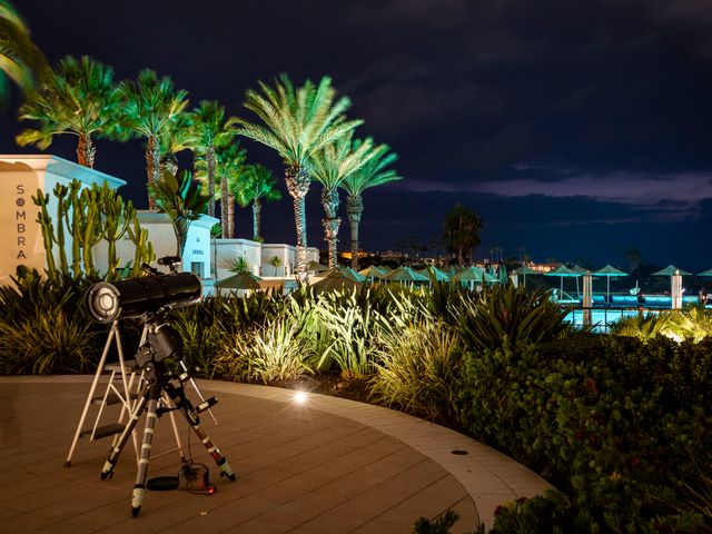 A deck with a telescope on it at night surrounded by palm trees next to a pool area.