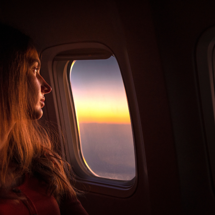 A woman sits at a plane window watching the sunrise.