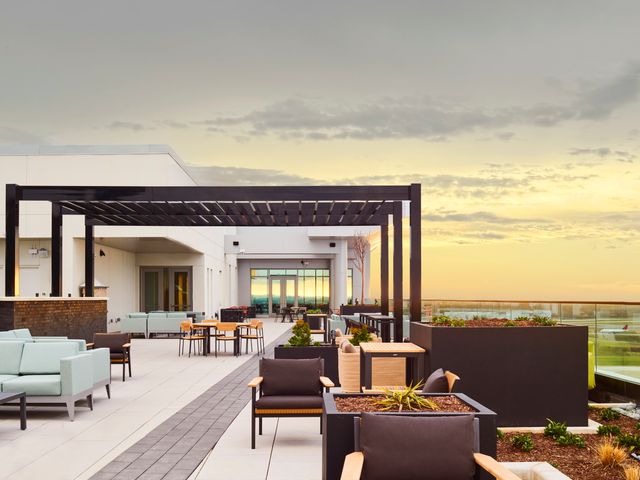 A modern looking hotel rooftop with seating areas, a pergola, and city views in the distance. 