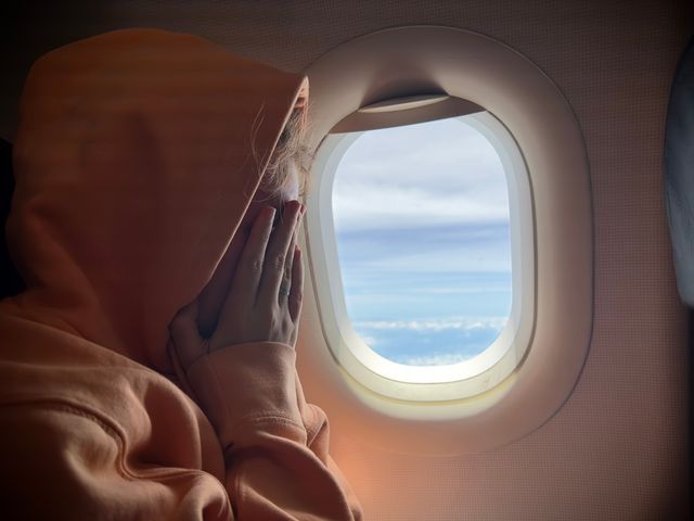 A person on an airplane next to a window covering their face with a hood on.