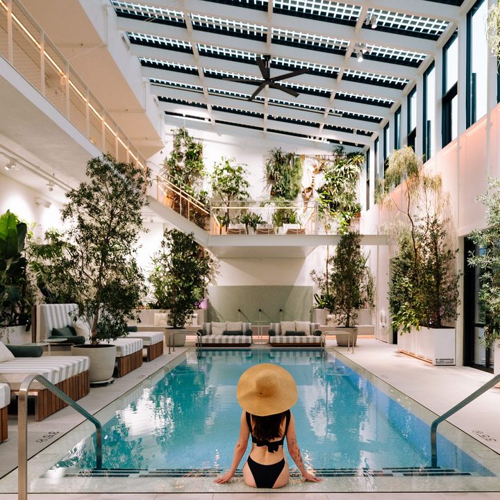 A woman sits facing an indoor pool as seen from behind wearing a hat.