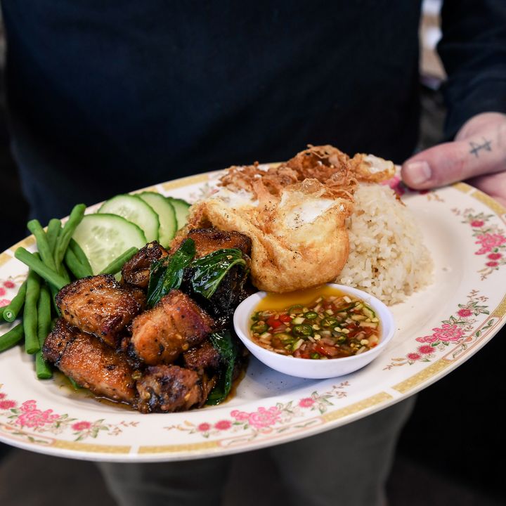 Hands serving a dish of food at Eem in Portland, Oregon.