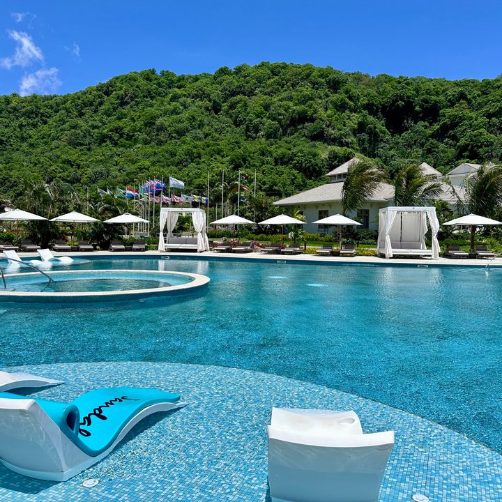 A sprawling lagoon-style turquoise pool with in-water chaise lounges, one of which says Sandals Resorts on it.