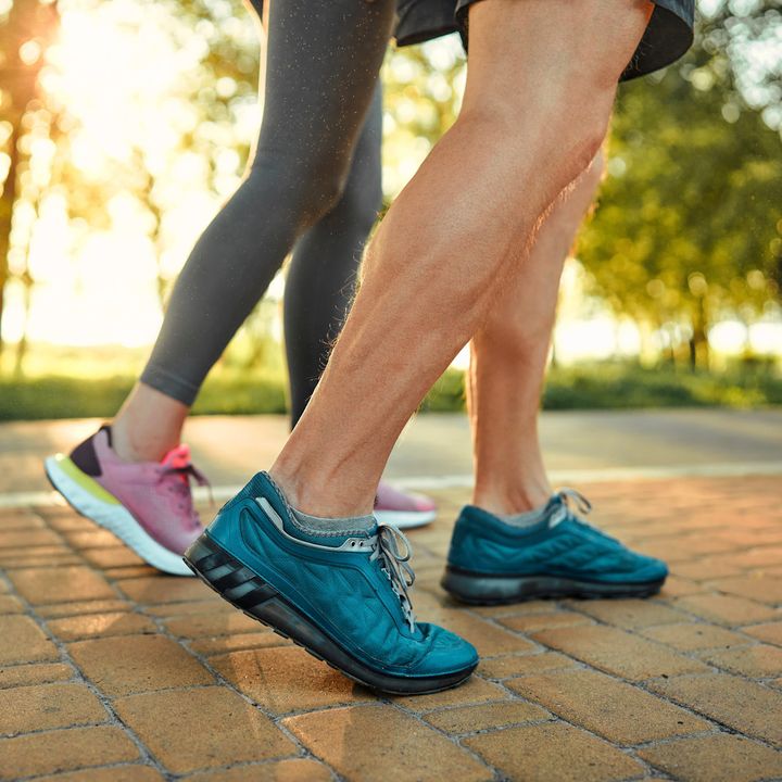 Close up of male and female legs in blue and pink sneakers on a cobblestone path in a park.
