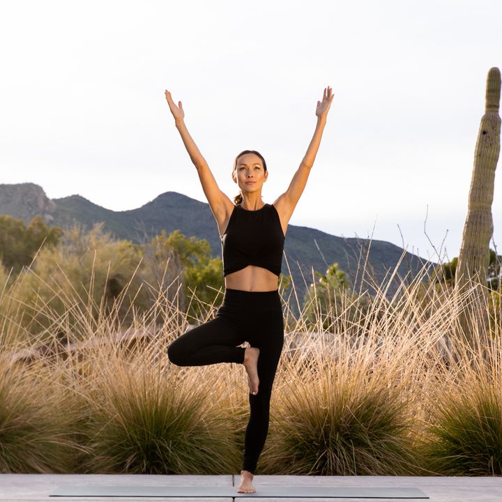 A woman is seen doing yoga in tree pose in a desert setting at Civana resort.