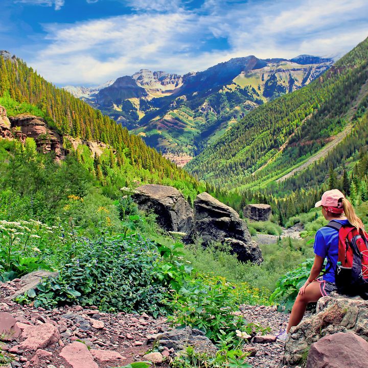 A hiker rests on a rock at the top of the Bear Creek Trail in Telluride, Colorado, during summer.