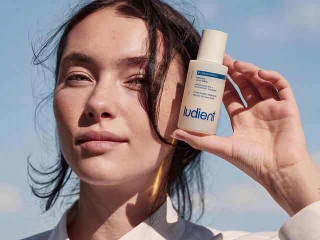 A woman holds up a small white bottle of serum next to her face.