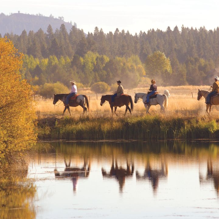 A group of horseback riders next to a river and fall foliage at Sunriver Resort in Oregon.
