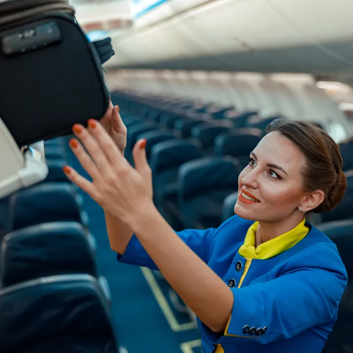 A flight attendant loads a suitcase into an overhead compartment.