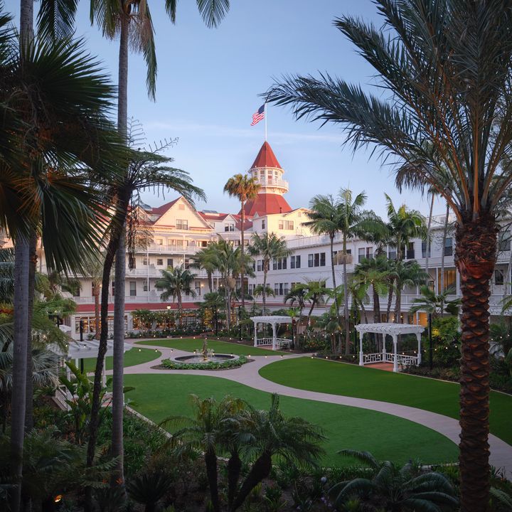 The Victorian Building at Hotel Del Coronado as seen through the middle of palm trees with a lush green lawn.