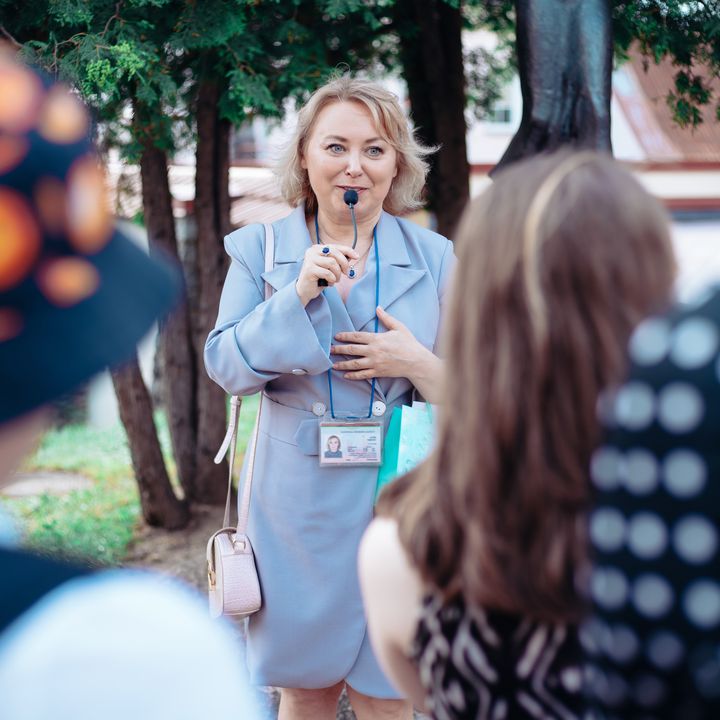 A female tour guide wearing a name tag speaks into a microphone while addressing a group.