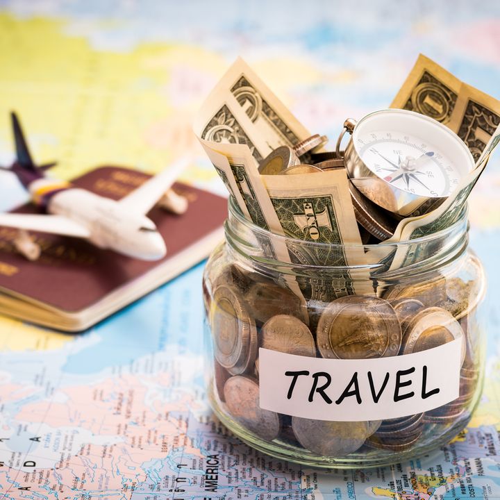A toy plane sitting on top of a passport next to a jar filled with change and dollars labeled travel, all on top of a map.