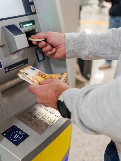 A person at an ATM with only arms visible taking out Euros.