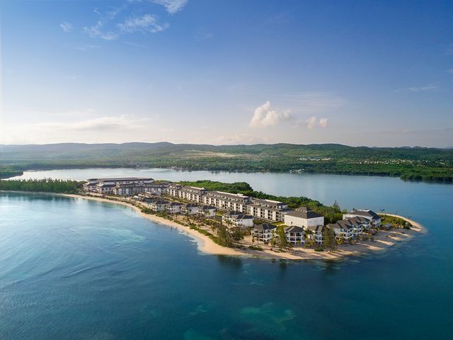 An aerial view over a beach hotel jutting out on a peninsula surrounded by water.