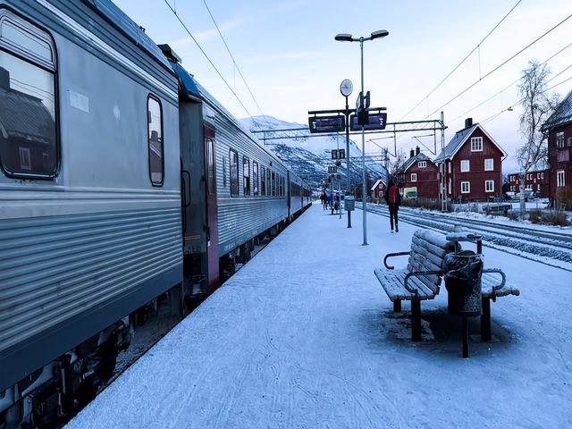 A snow covered train stop with benches and mountains in the distance.