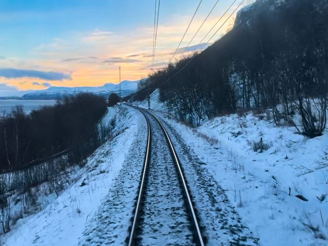 Train tracks on a snowy landscape surrounded by bare trees.