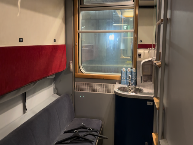 A train cabin with bench seating, a sink, and a window.