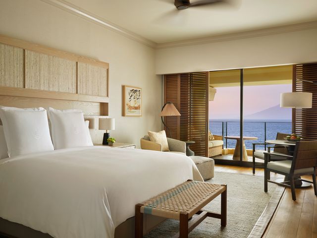 A guest room at the Four Seasons Resort Maui with a bed, seating area, and ocean views through the patio doors leading to a lanai.
