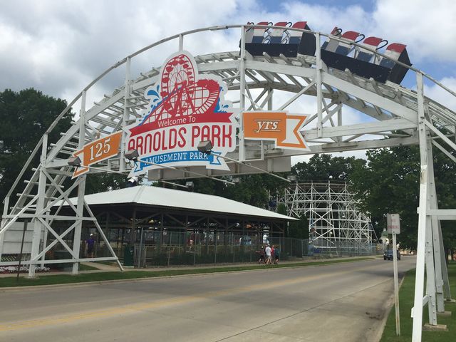 The entrance sign to Arnold's Park with a celebration of 125 years and an arched rollercoaster over the top of the sign without passengers