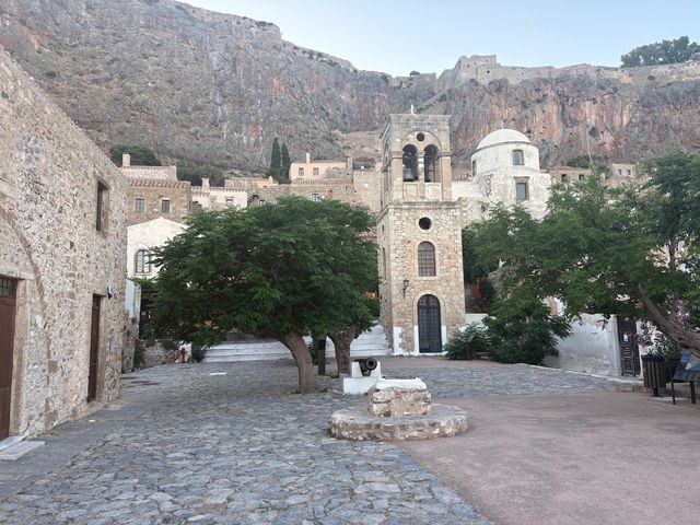 A city square in Monemvasia, Greece, with stone walls and cobblestone streets.