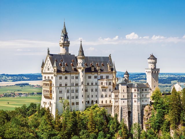 The famous Neuschwanstein Castle in Bavaria, Germany surrounded by trees and a green countryside.