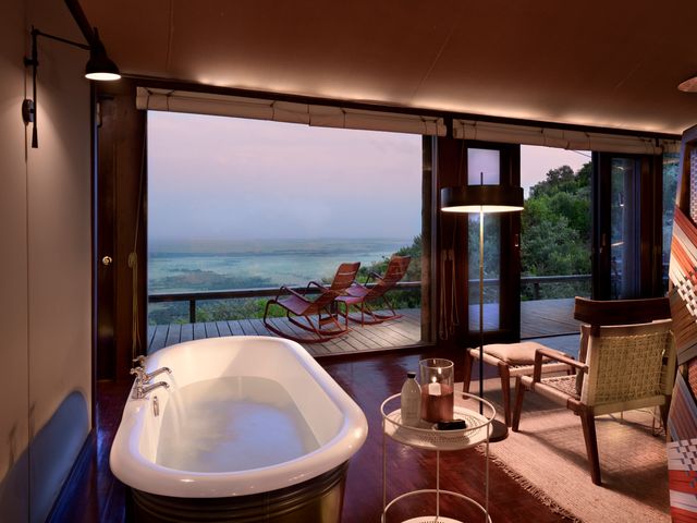 A tented suite with a soaking bathtub, seating area, and a deck overlooking stunning scenery.