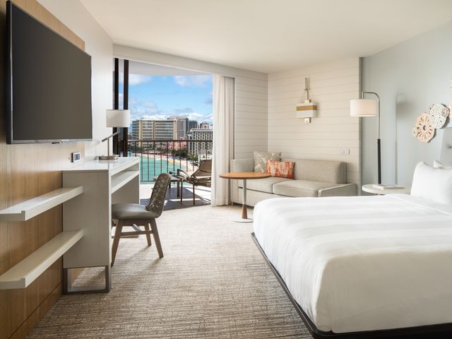 A hotel room at Waikiki Beach Marriott Resort & Spa with ocean views out the balcony, a king-size bed, a desk and chair, TV, and a couch.