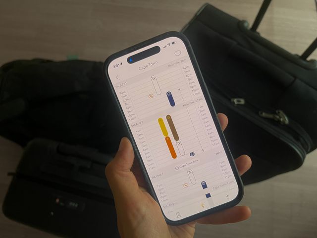 A hand holding an app with a color-coded schedule next to luggage.
