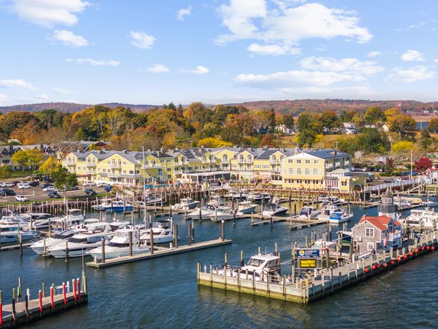 An aerial view over a yellow and white hotel facing a marina surrounded by fall foliage trees.