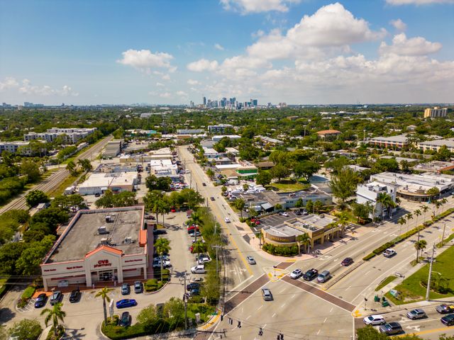 An aerial view over a suburban area with commercial businesses and houses with a city in the far distance and a flat landscape.
