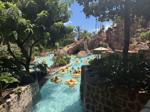 A lazy river with faux rock formations around it filled with people in yellow tubes.