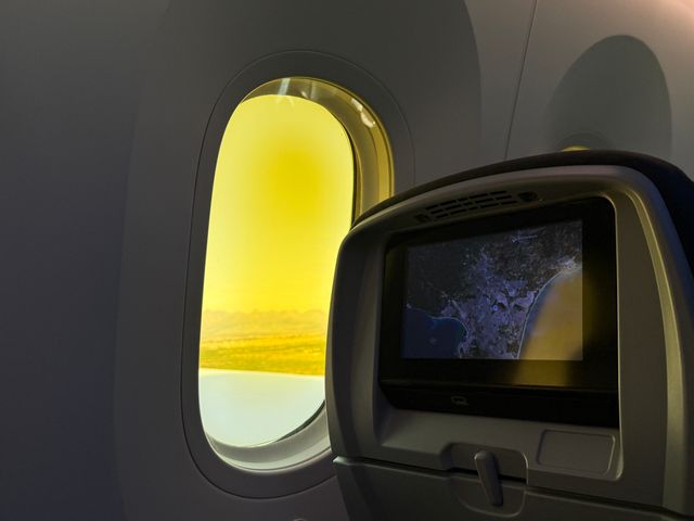 An airplane window seat with a map on the screen in front and the window open with golden light.