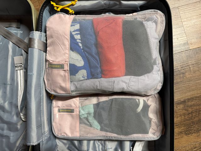 An open suitcase with two packing cubes on one side that have mesh and pink fabric.