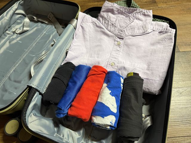 An open suitcase with clothes on one side, half of which are folded and smaller items are rolled.