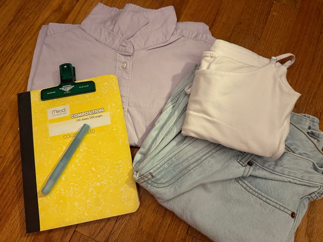 A folded 3-piece outfit laid out on a wood surface with a notebook and pen next to it.