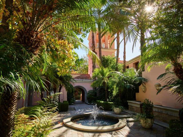 A courtyard with a fountain surrounded by pink stucco walls and lush greenery.