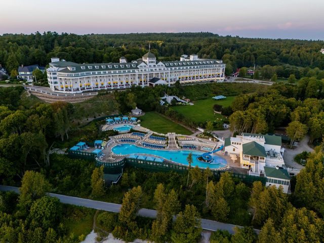 An aerial view over Grand Hotel on Mackinac Island with a large pool area surrounded by trees. 