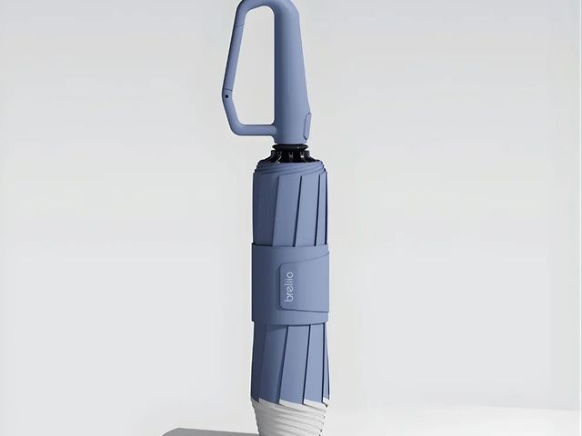 A blue umbrella with white edges standing on a table with the handle up in the air, against a white background.