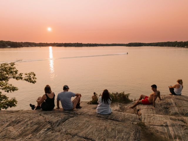 People gathered cliffside to watch the setting sun over Muskoka lake at dusk.