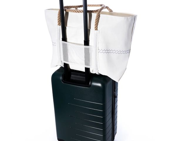 A large tote bag positioned on top of a rolling suitcase, secured with a trolley sleeve, against a white background.