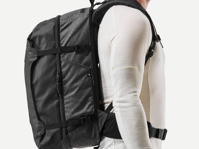 A man is visible in profile, from the chin to mid-body, wearing a black backpack against a white background.